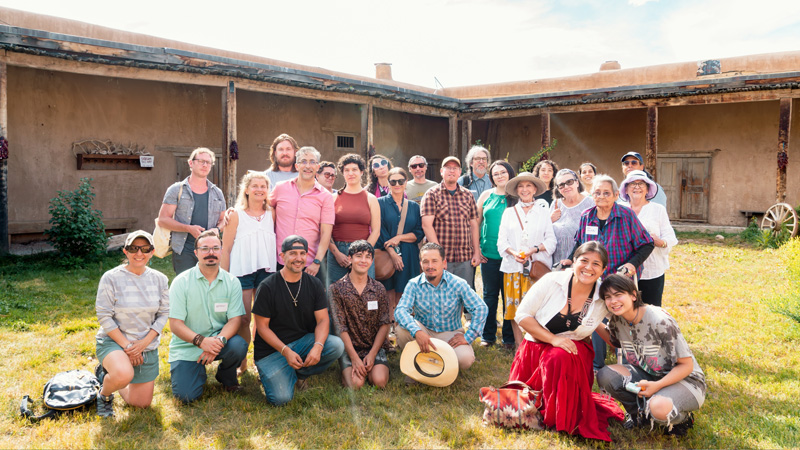 a group of people posing for a photo in front of a traditional native housing